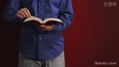 一名男子靠在一堵红墙上，翻着书页读圣经，然后把手伸进口袋